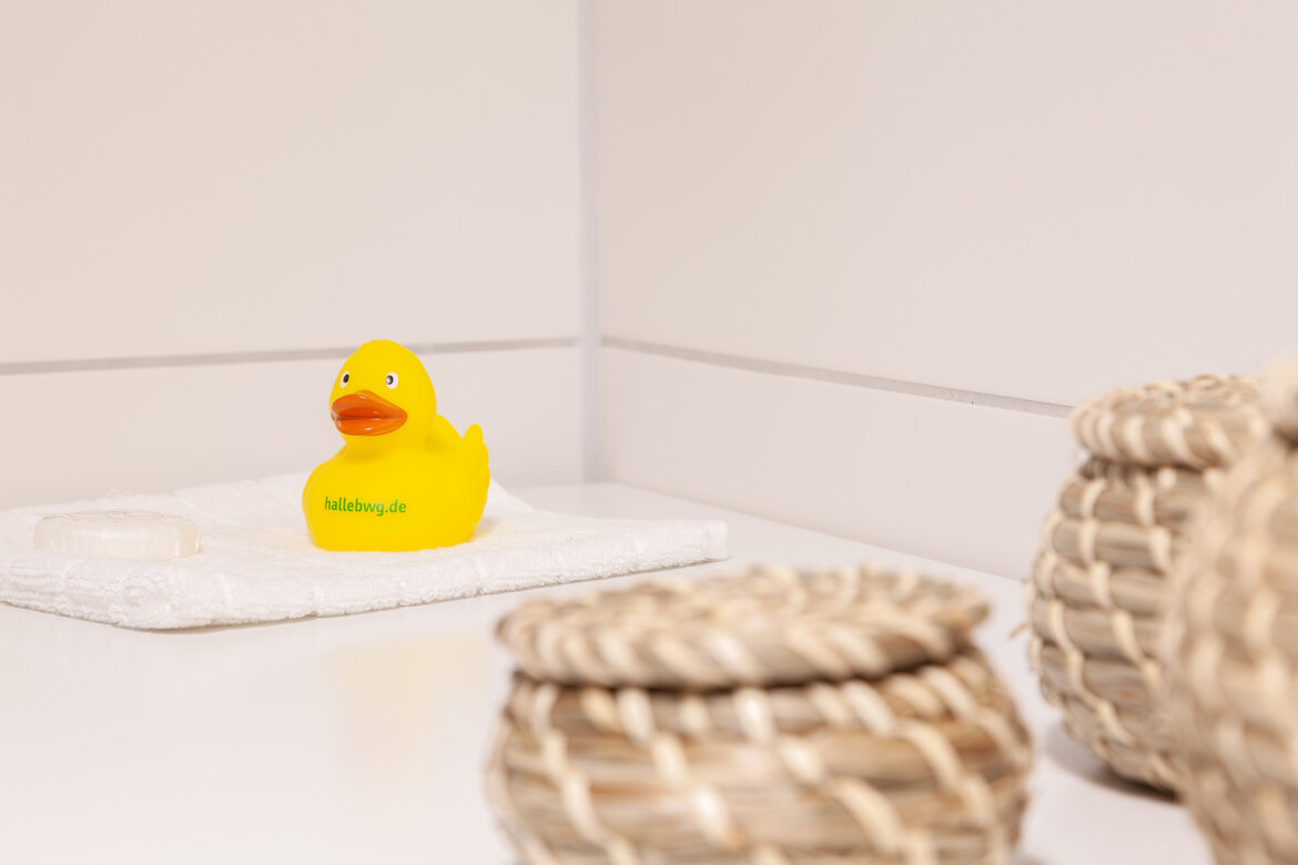 BWG-Ente auf weißer Badarmatur mit zwei geflochtenen Körben im Vordergrund