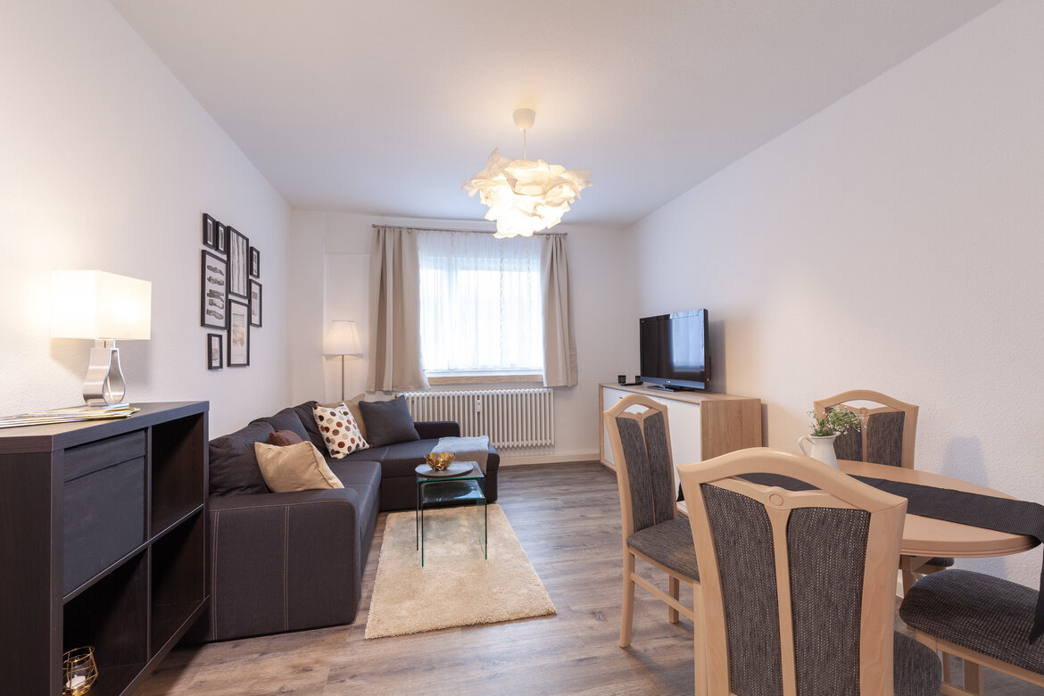 Essbereich mit vier Stühlen um runden Tisch und Sofa-Ecke im Hintergrund