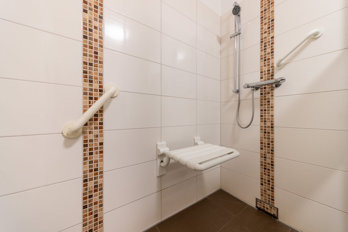 Ebenerdige Dusche mit mehreren Haltegriffen und einer Sitzmöglichkeit