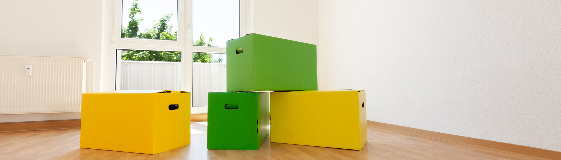 Zwei grüne und eine gelbe Kiste gestapelt in einer sanierten, hellen Wohnung